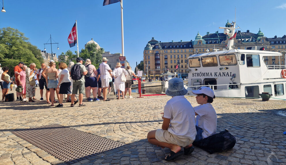 Två barn i skuggan på Nybrokajen i Stockholm, i väntan på ombordstigning på MS Strömma kanal