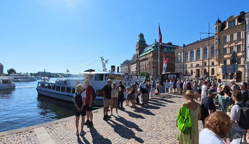 Köande båtgäster på Nybrokajen med Strömma-fartyg i bakgrunden